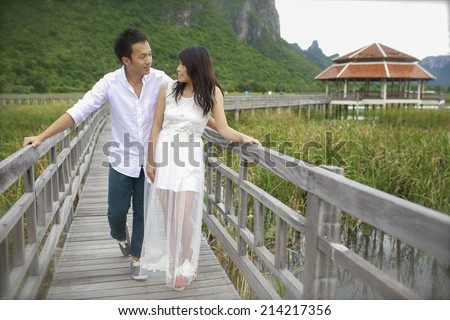 The groom and the bride standing on the wooden bridge by the lake and looking at each other.