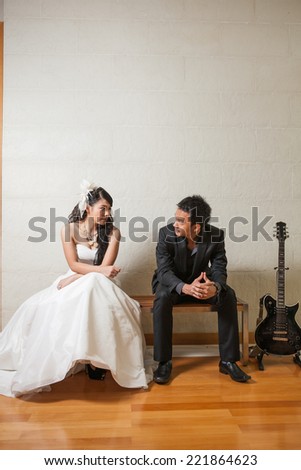 Bride and groom happy sitting on the wooden bench with back guitar on white background.