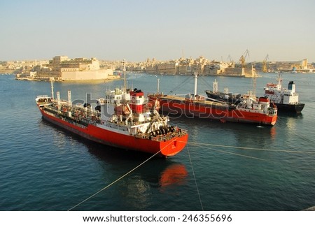 Three large boats in Maltese port, reflected in water with historical buildings in the background