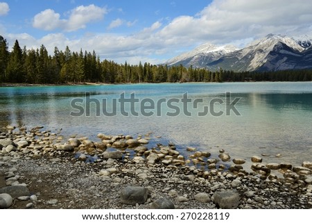 Rocky Shoreline of Lake Edith, Crystal Clear Water with Mountains and Evergreen Forest in Background