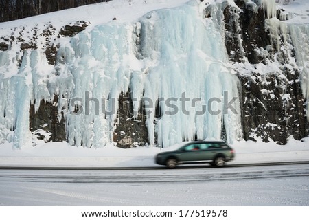 Moving car on winter road against frozen waterfall in Norway.