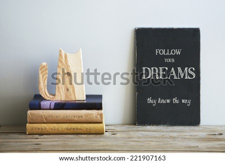 motivational quote  FOLLOW YOUR DREAMS on chalkboard with books and wooden cat