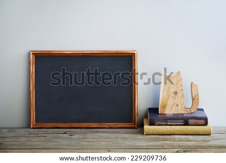 chalkboard frame on the grey wall with books and wooden cat. Place for text. Scandinavian or American style interior.