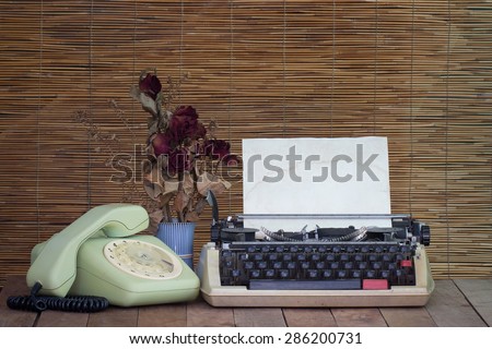 Still life with old typewriter telephone with dry rose flowers on wooden table