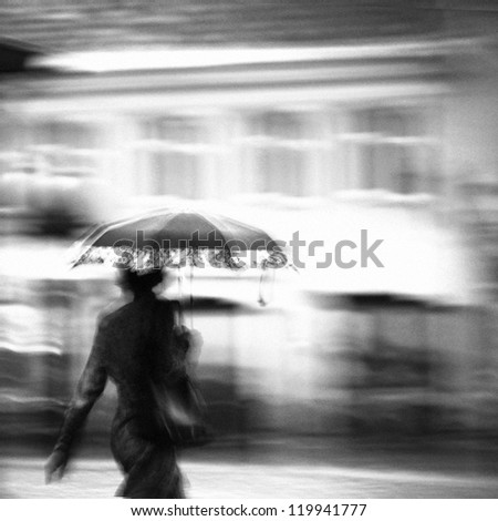 Woman in a rain walking with umbrella. Unrecognizable person in motion blur.