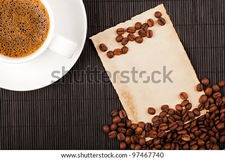 Coffee cup, coffee crops and handmade paper placed on bamboo coaster. Place for text.