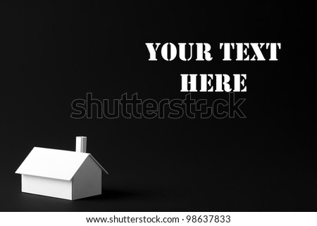 Minimalistic concept image of a small simple white model house with black background for copy space.