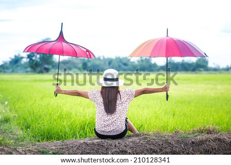 Beautiful woman holding multicolored umbrella in green rice field and sunset. Vintage