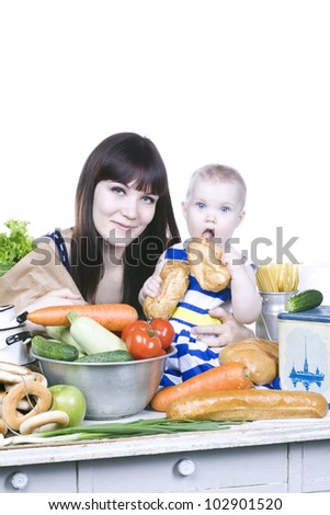 a little girl sitting on a table in the kitchen and eat bread, sitting next to Mom