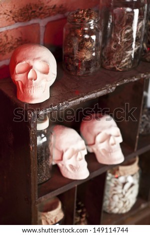 three skulls and a lot of jars of dried herbs on the shelves illuminated with red light on the old kitchen