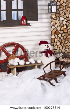 snowman in a hat and a scarf standing on the street in front of wall of a country house