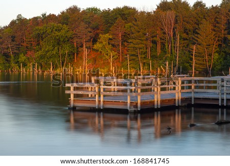 Peaceful Setting Of Pier On A Calm Lake With The Morning Light Shining On Autumn Trees In Central Iowa
