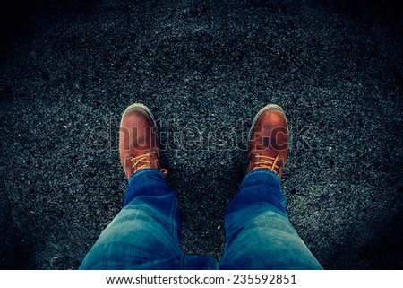 Male feet in jeans and boots on asphalt