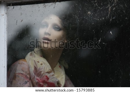 Female mannequin gazing through dirty window.