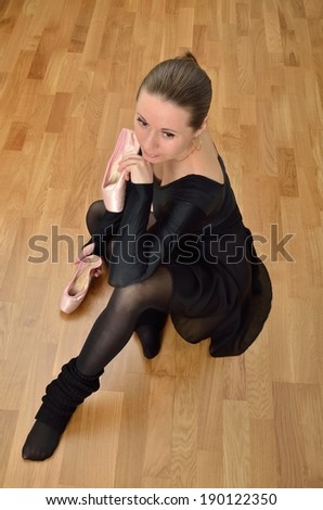 Ballerina in black sitting on the floor with ballet pointe shoes in hands