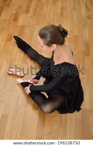 Ballerina in black sitting on the floor and trying on a pointe