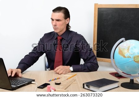 Rigorous teacher serious male at table working on a computer