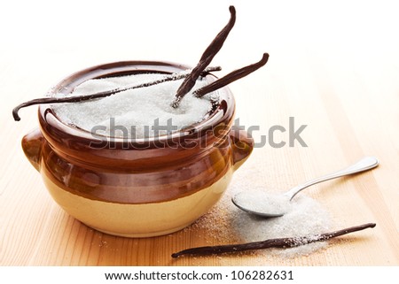 Brown bowl with white vanilla sugar, vanilla beans and a spoon on wood