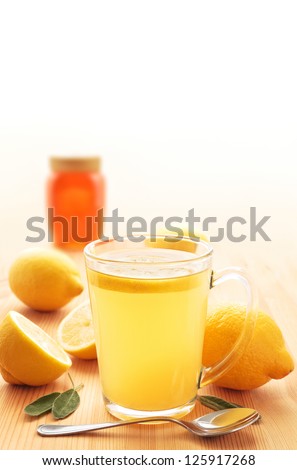 Hot lemon drink in a glass mug on wood with honey, lemons and sage leaves