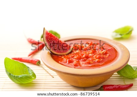 Fresh hot Asian chili sauce in a brown bowl decorated with a piece of fig, chili peppers and basil leaves