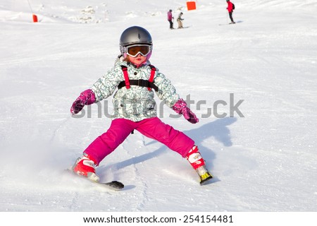 Young girl in ski mask learning skiing on snow downhill. First ski lesson.
