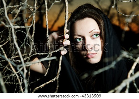 East beauty with green eyes in a black scarf on a decline makes the way through trees