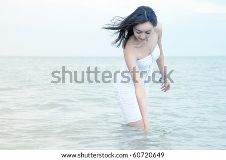 The girl with a flowing hair in a white short dress costs knee-deep in water
