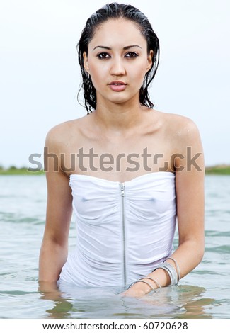 The attractive girl of the Asian appearance in a white wet transparent dress costs on a waist in water