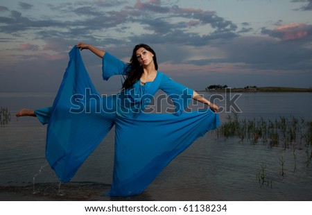 The beautiful girl in a dark blue dress poses in water in the form of the butterfly
