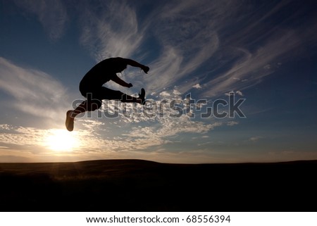 The silhouette of the guy against a decline, the beautiful sky, jumps upwards, a kick