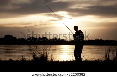 The silhouette of the guy with a fishing tackle, at sunset, which fishes