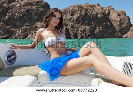 The beautiful girl sits on a sofa in a back part of a boat and poses on the sun