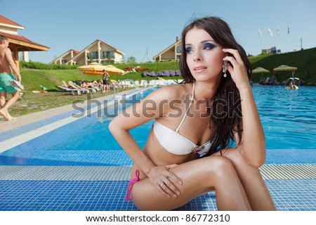 Portrait of the beautiful girl with a flower in hair sitting on the brink of pool