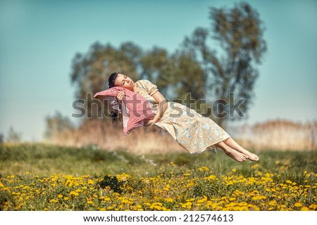 Girl hovers and sleeps on a pillow over a beautiful meadow.