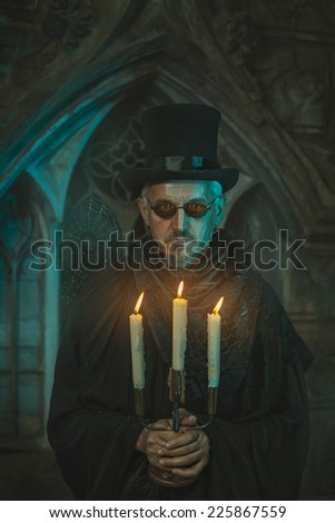 Strange and scary man standing with a candelabrum in which candles are burning. Men behind the old castle.