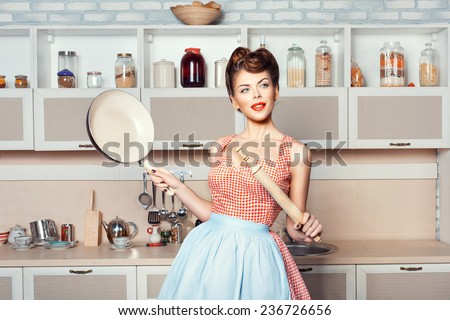 The girl in the kitchen in the hands holding pan and rolling pin.