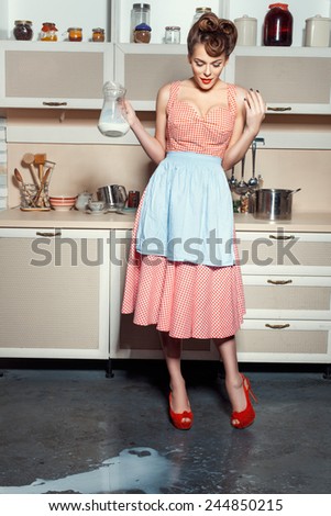 A woman is standing in the kitchen and looks at the floor. On the floor, spilled milk.