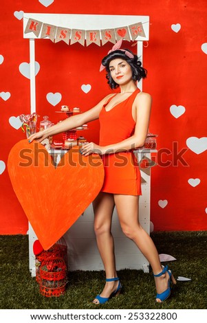 Beautiful retro girl in red dress and red paper heart in hands.