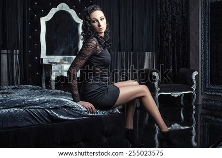 Beautiful girl with long legs sitting on the bed in the dark bedroom. The bedroom is richly furnished. Photo Tinting in cool shades.
