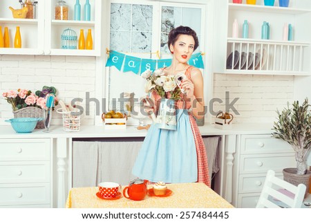 Pin-up style. Girl in retro style apron stands in the kitchen, but in the hands holding flowers.