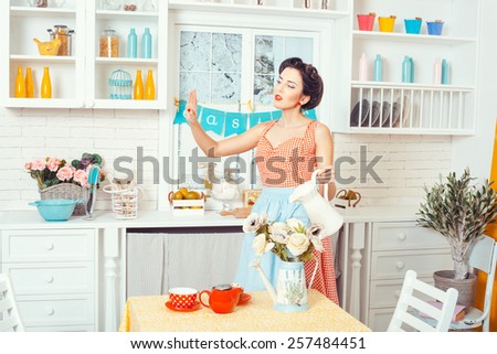 Pin-up style. Woman in an apron in the kitchen stands and watering flowers. Look at her nails on the arm.