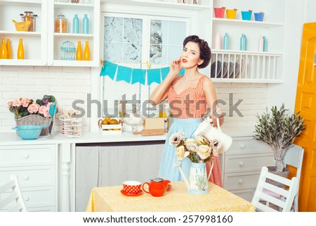 Pin-up style. Girl watering flowers standing in the kitchen in a retro style.