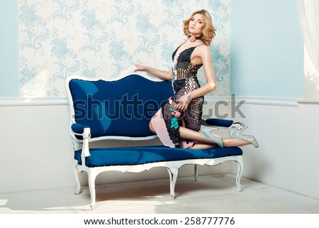 Girl standing knees on the sofa and posing. She knitted dress decorated with flowers.