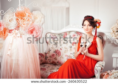 Tender girl with big eyes sitting on a sofa and holding pointe shoes, ballet dress hanging next.