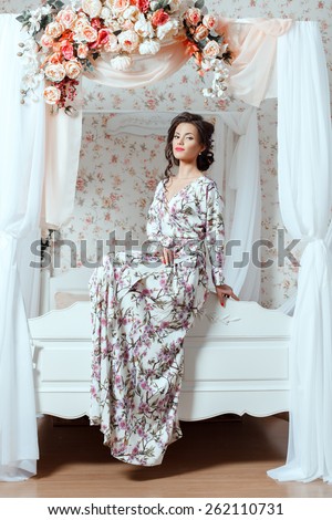 Cute girl smile sitting on the back of the bed. Bed with a canopy and flowers.
