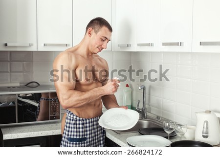 Man with big muscles standing in the kitchen and wash the plate.