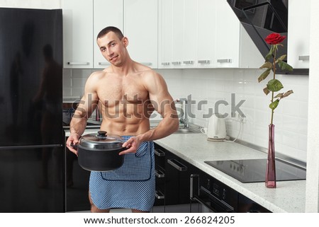 Man with big muscles in an apron with a pan in hand stands in the kitchen.