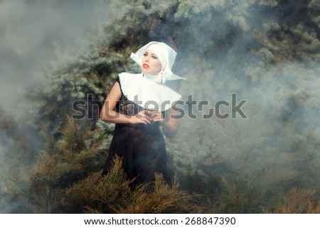 Beautiful glamorous nun looks up amid the smoke, in the background nature.
