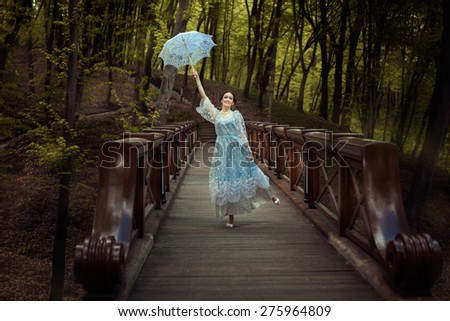 Young girl wants to fly to the umbrella. It is in the fairy forest standing on the bridge.
