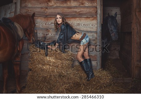 Beautiful girl standing near the stables on the straw beside her two horses.